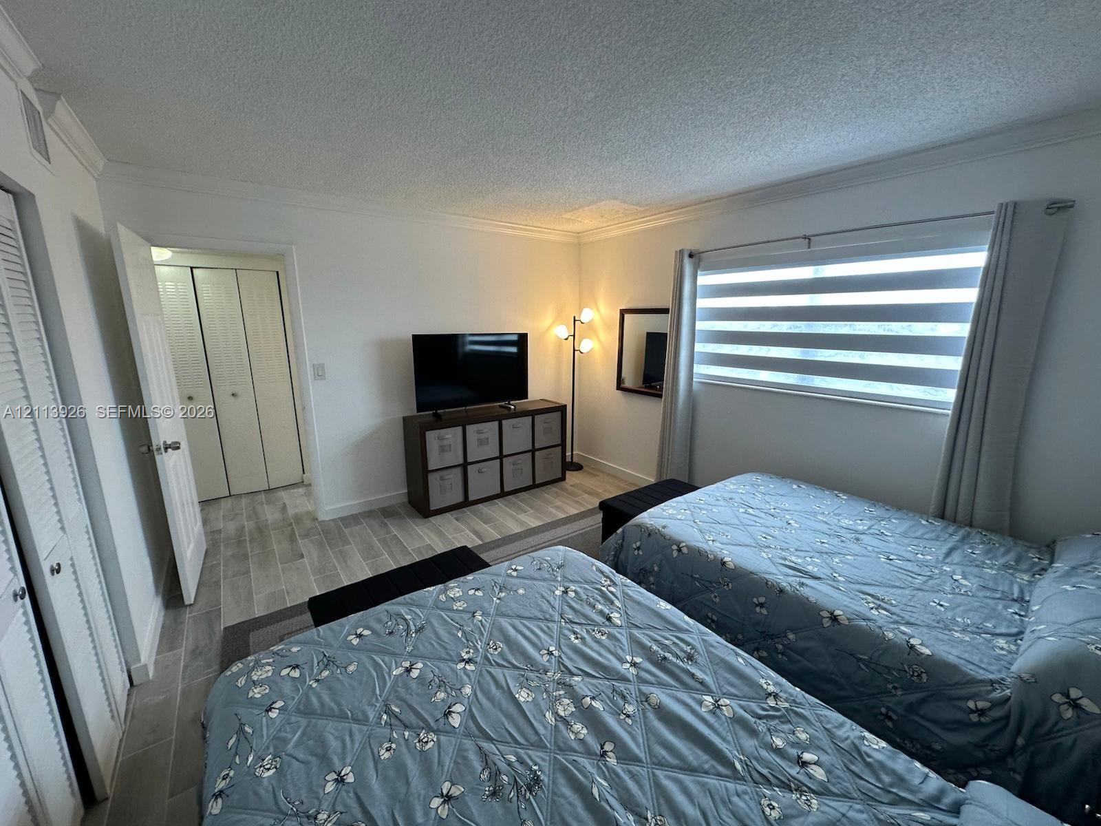 Room featuring wood-finish tile flooring, dual-panel closet doors, textured ceilings, and striped privacy window shades