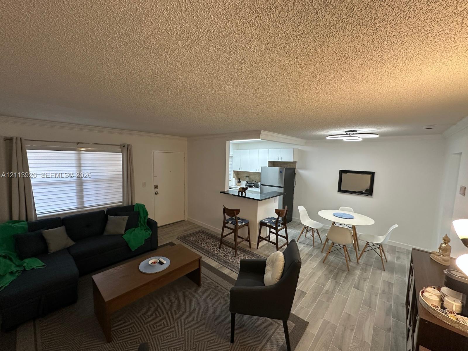 Open-concept interior featuring wood-finish flooring, a kitchen breakfast bar with countertop seating, and a modern circular LED light fixture