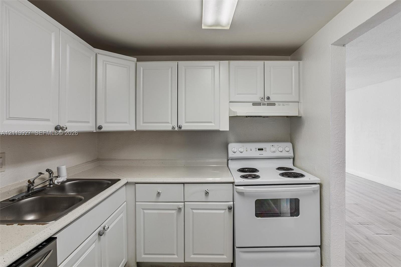 Kitchen featuring white shaker-style cabinetry, solid-surface countertops, dual-basin stainless steel sink, and a white electric range with an integrated hood