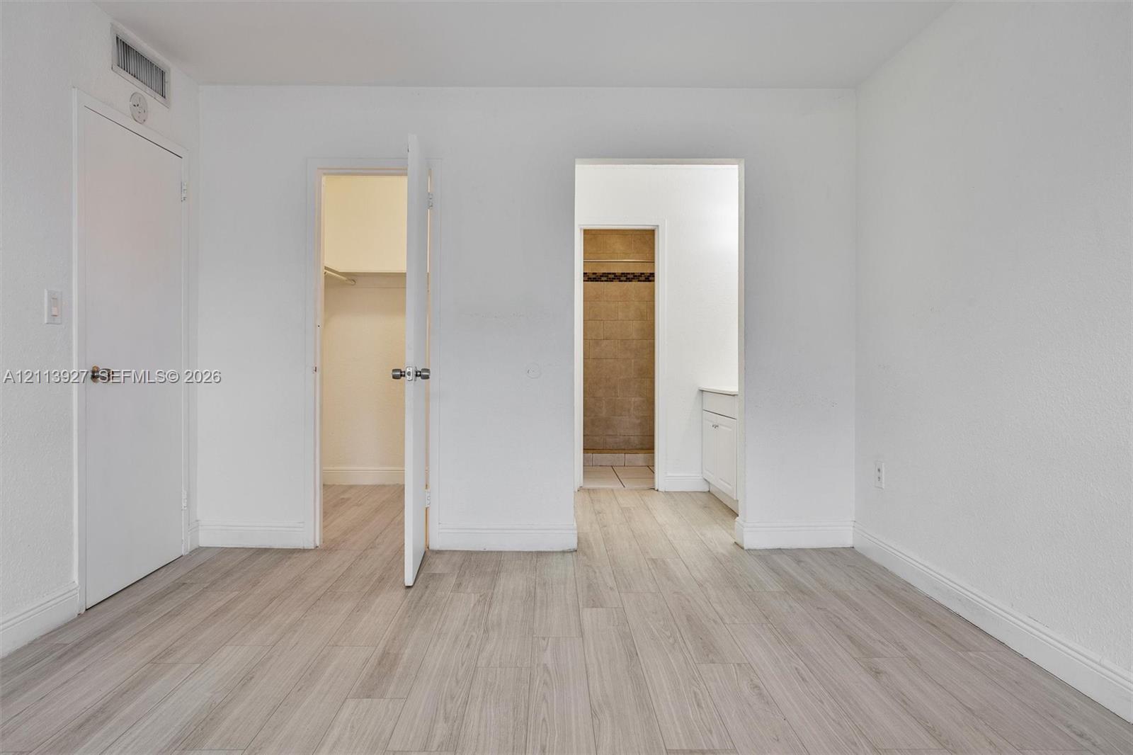 Neutral-toned wood-finish flooring, walk-in closet with built-in shelving, and vanity with stone-finish countertop