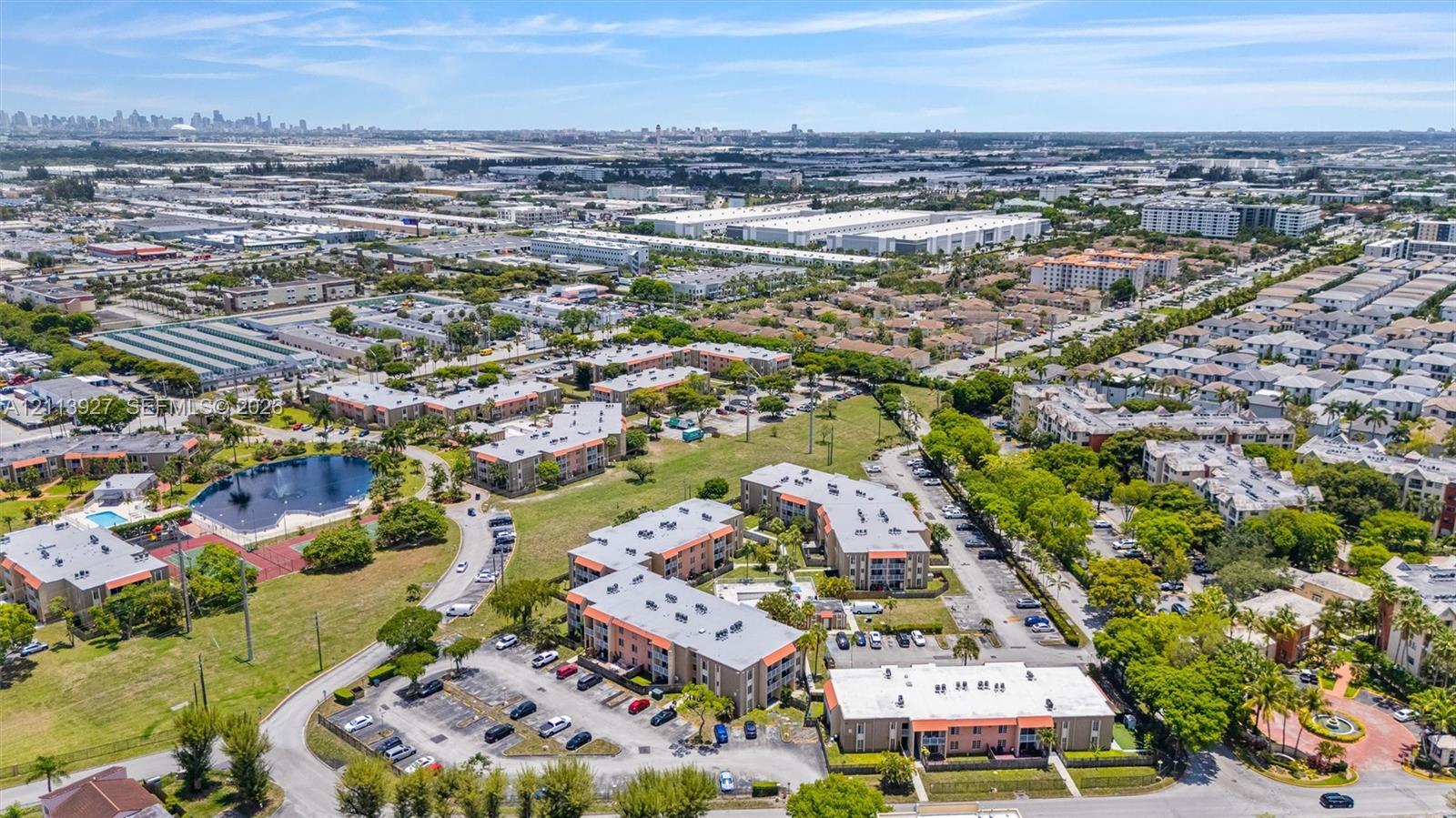Aerial perspective featuring multi-story residential buildings, surface parking areas, on-site pond, and landscaped green space