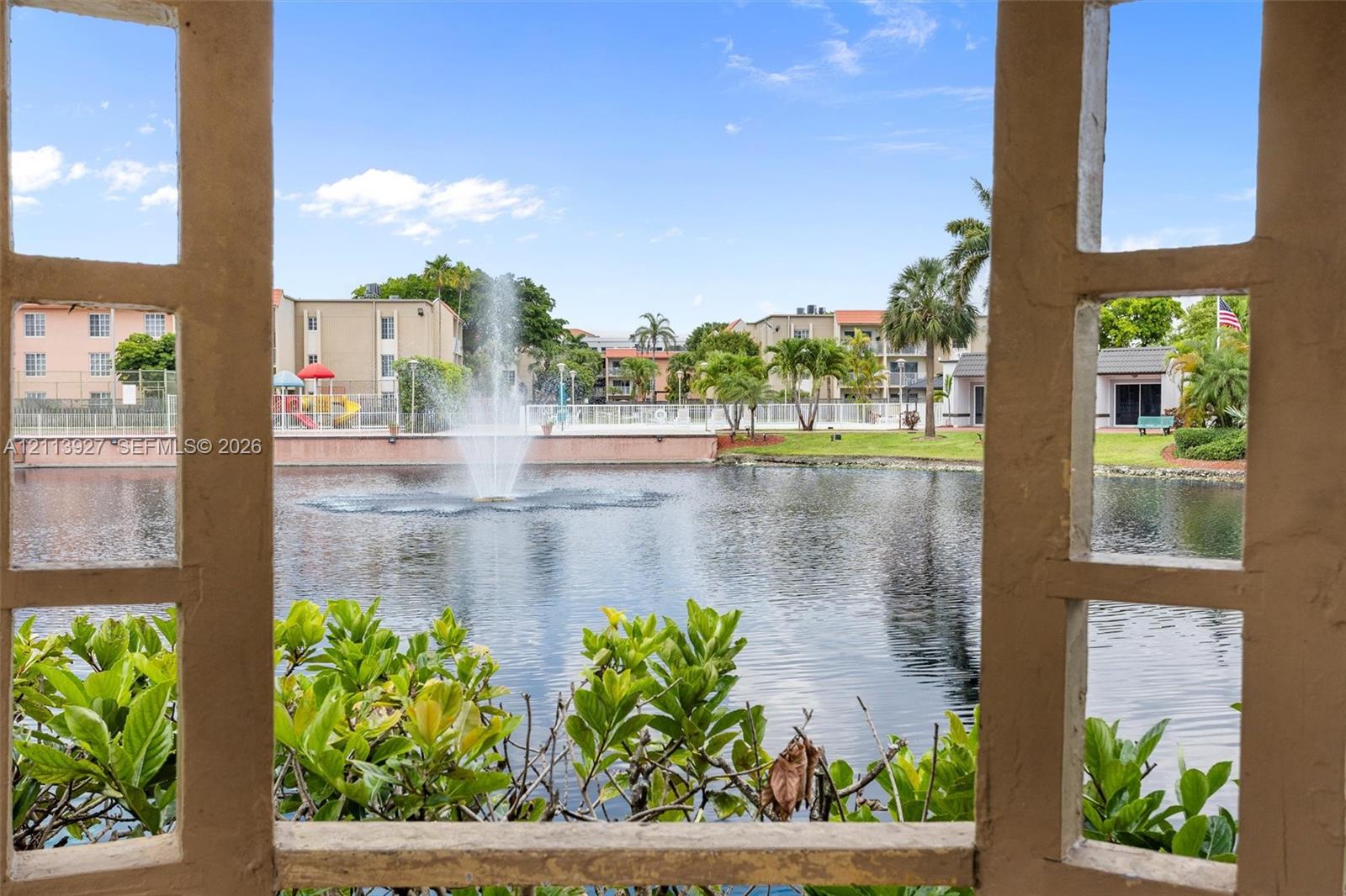 Stucco-framed gazebo structure overlooking a central pond featuring a built-in fountain, perimeter landscaping, and established palm trees