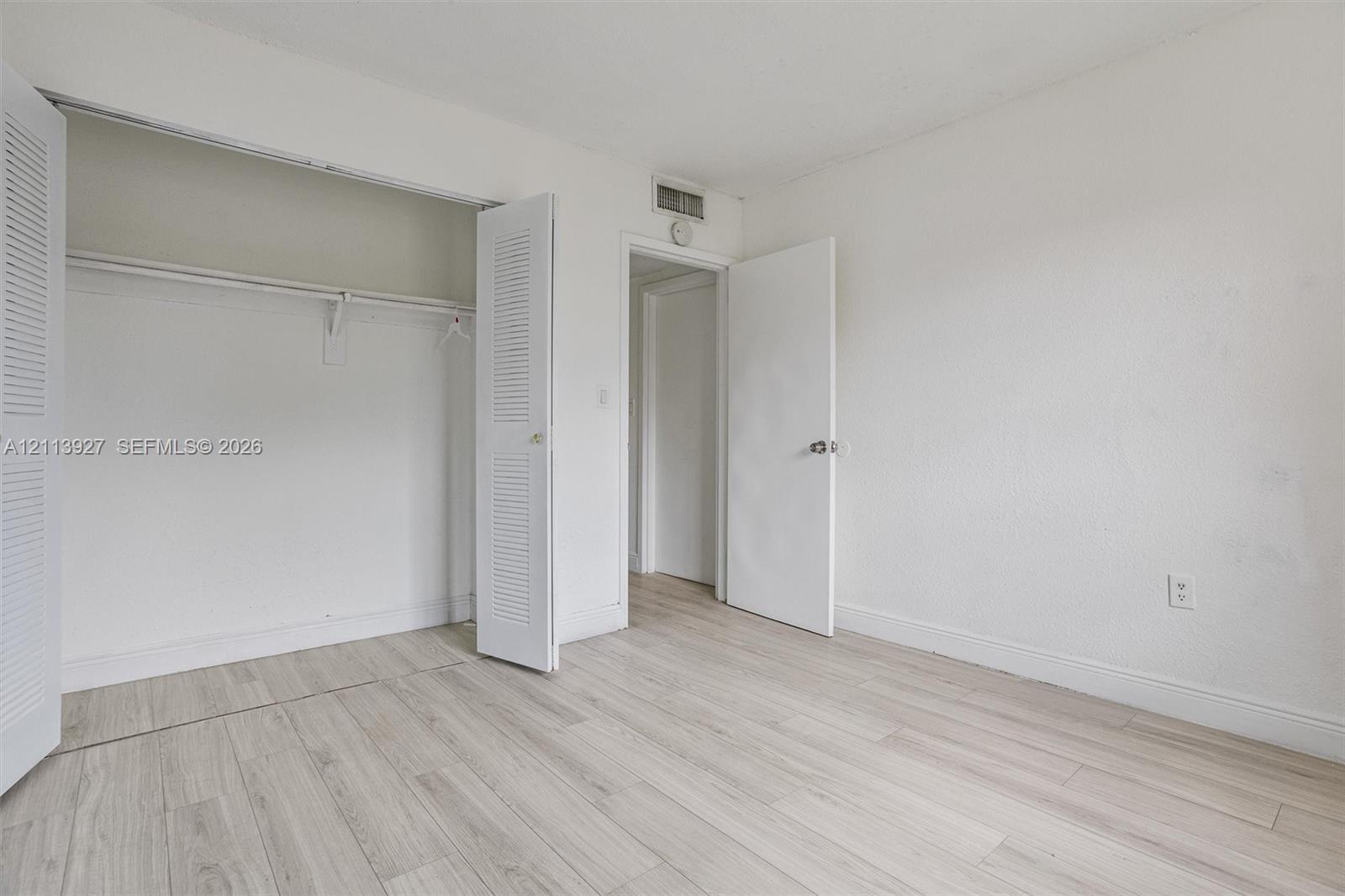 Room featuring wood-finish flooring, white walls, and a closet with dual louvered doors