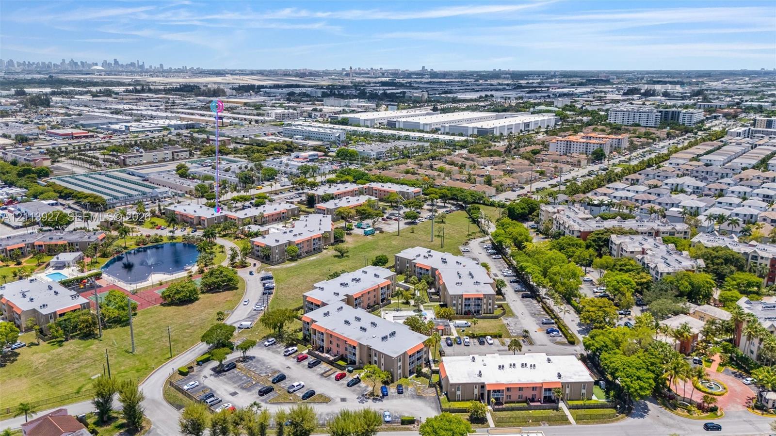 Aerial perspective of a multi-building residential complex featuring surface parking areas, landscaped grounds, and a central water feature