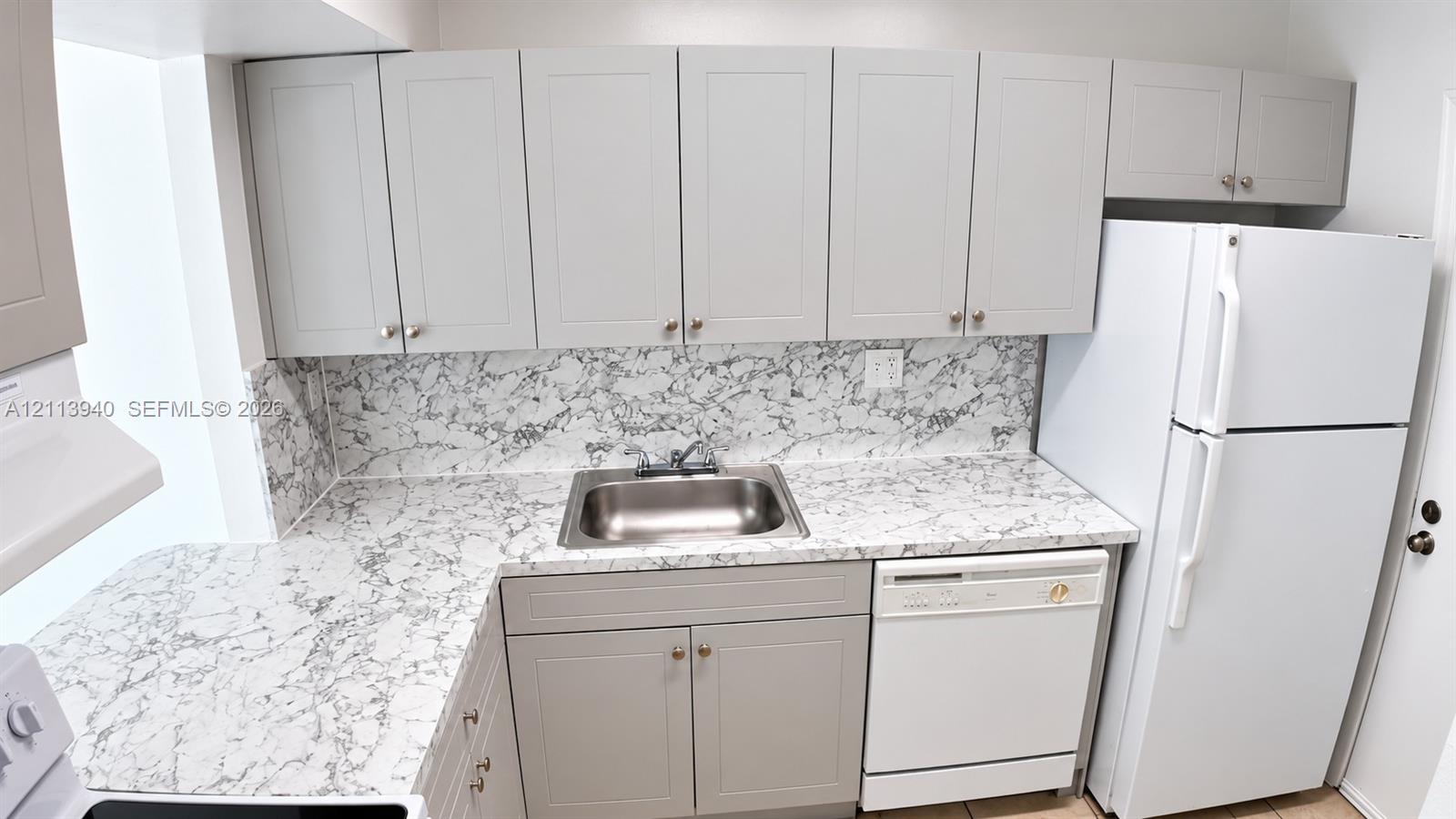Kitchen featuring shaker-style cabinetry, patterned stone-look countertops, matching full-height backsplash, stainless steel drop-in sink, and a built-in dishwasher