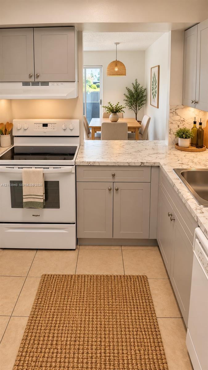 Kitchen featuring grey shaker-style cabinetry, white appliances, stone-patterned countertops, and tile flooring
