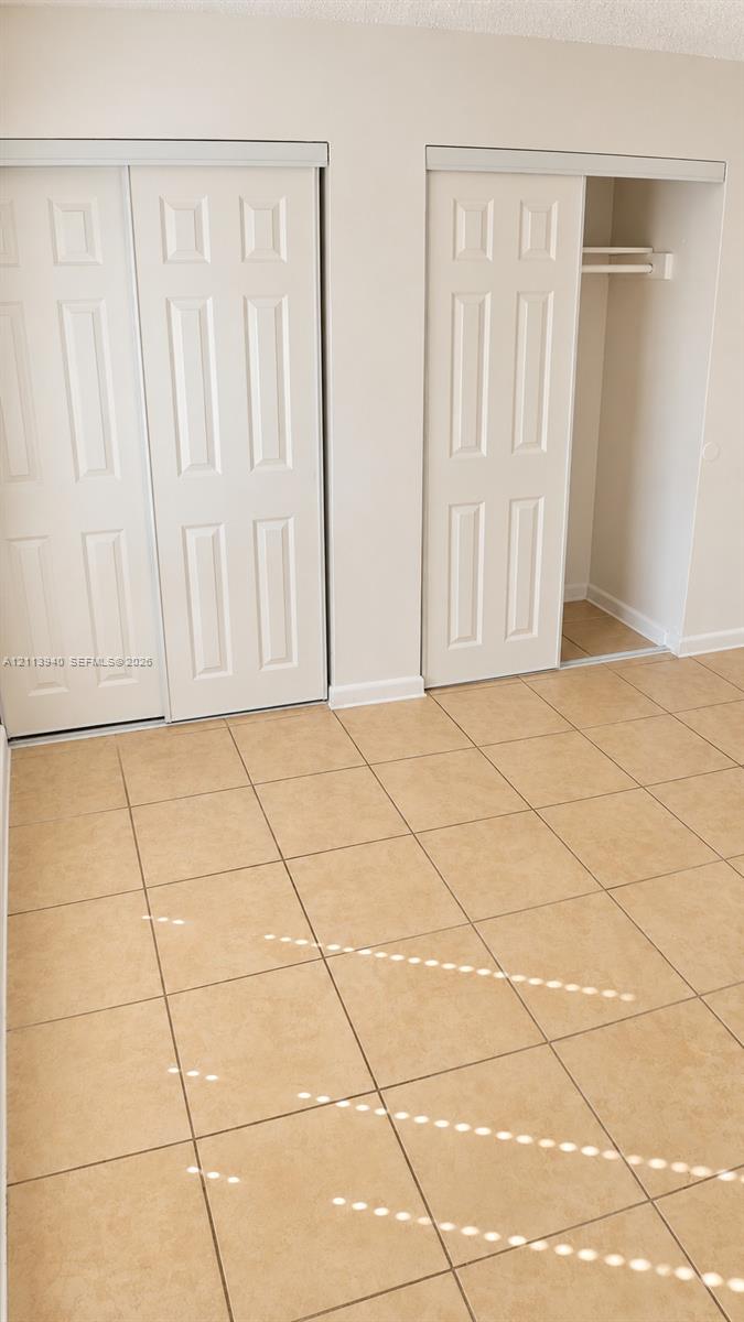 Neutral-toned ceramic tile flooring, two closets with six-panel sliding doors, and built-in closet shelving