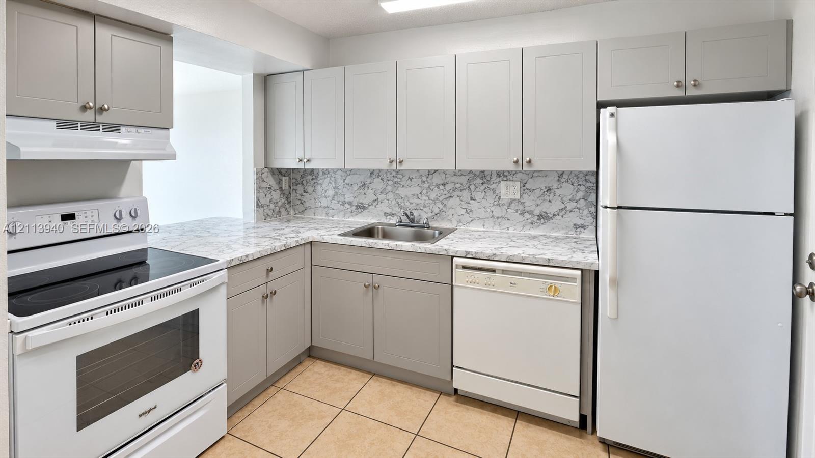 Kitchen featuring light gray shaker-style cabinetry, stone-patterned laminate countertops, tile flooring, and white built-in appliances including a range, dishwasher, and refrigerator