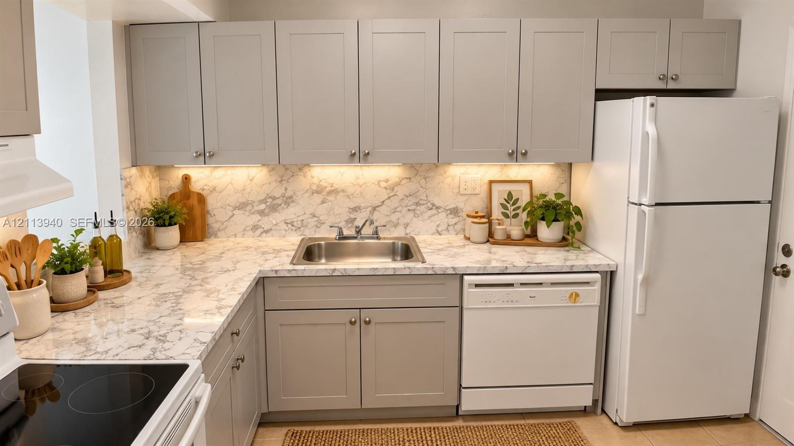 Kitchen featuring grey shaker-style cabinetry, stone-patterned countertops, integrated under-cabinet lighting, a stainless steel sink, and a white dishwasher
