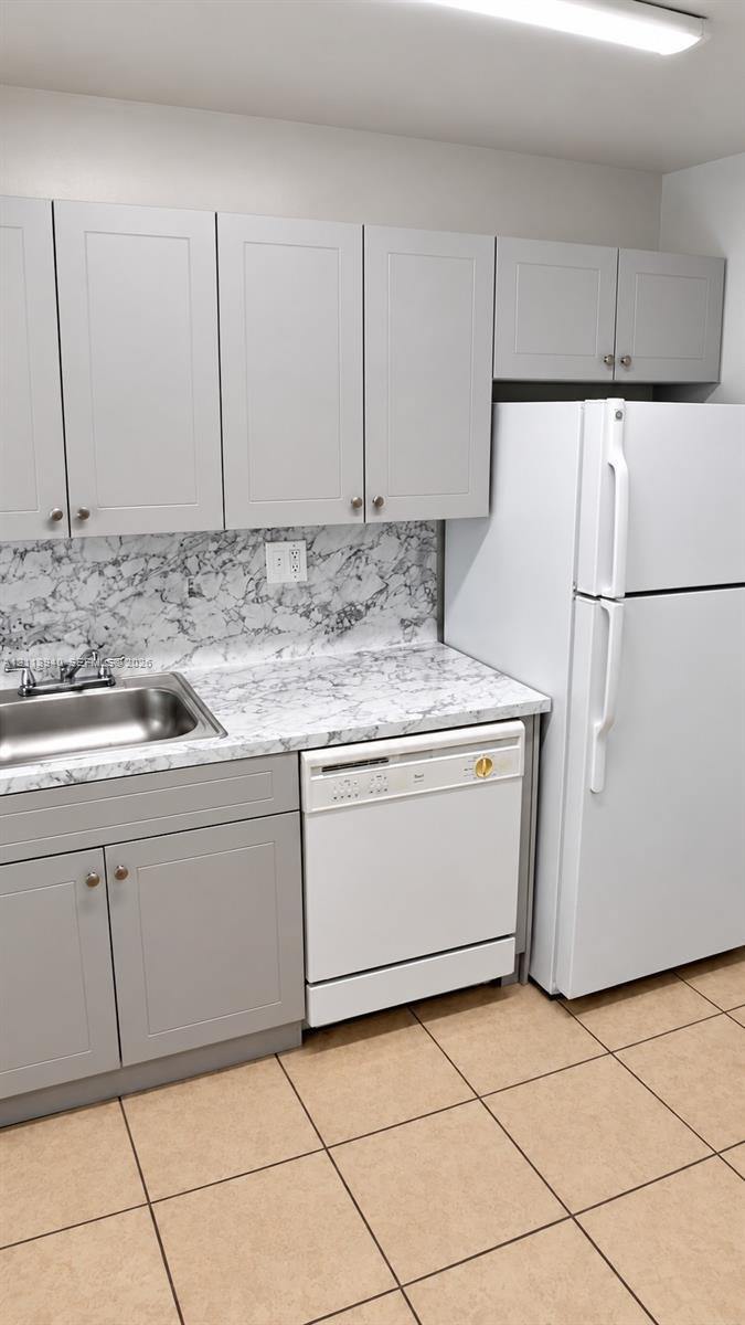 Shaker-style cabinetry in a neutral finish, stone-patterned laminate countertop, stainless steel sink with dual-handle faucet, integrated dishwasher, and ceramic tile flooring