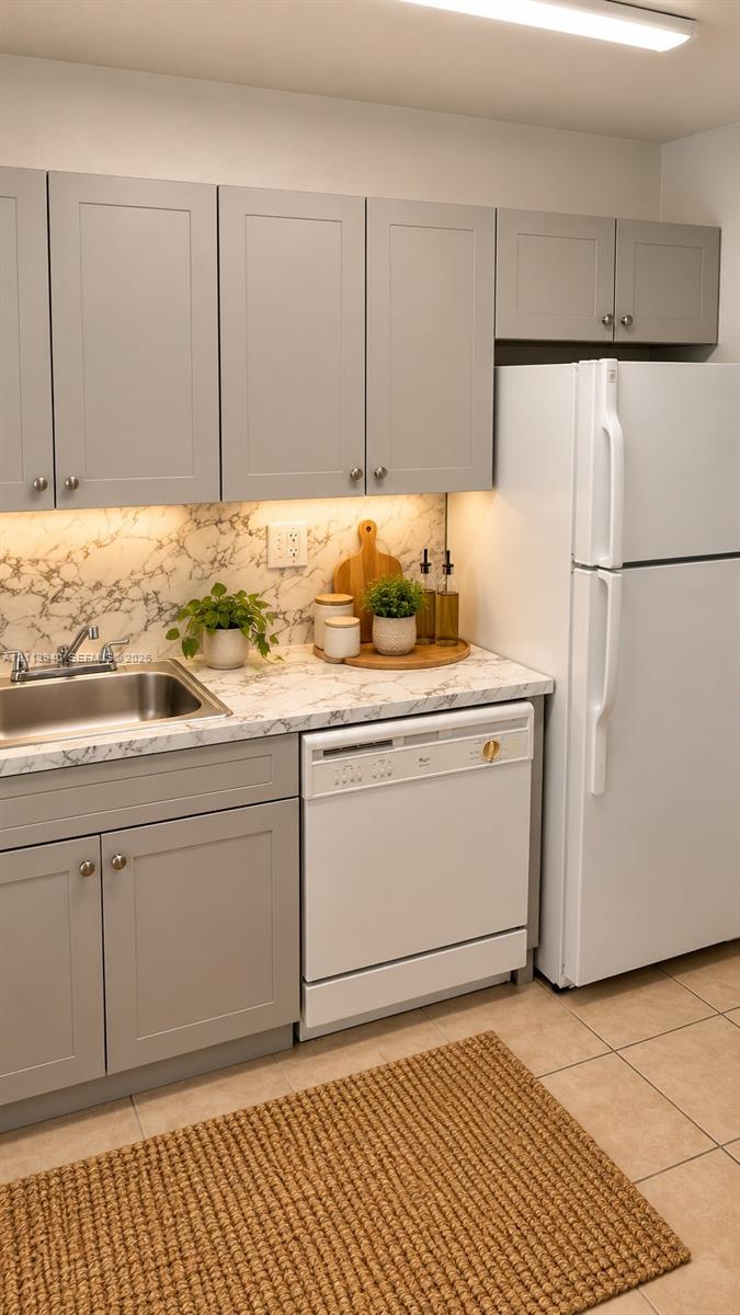 Kitchen featuring gray shaker-style cabinetry, stone-patterned countertops, a stainless steel undermount sink, and tile flooring