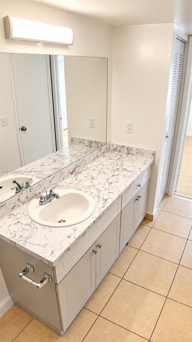 Vanity featuring a stone-patterned countertop, dual-basin undermount sinks with metallic fixtures, light-toned cabinetry, and large-format tile flooring