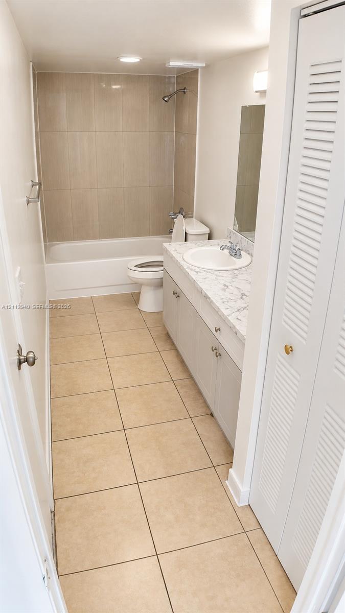 Bathroom featuring neutral floor tiling, a vanity with a stone-finish countertop and integrated sink, a full-wall mirror, and a tub-shower combination with floor-to-ceiling surround tile