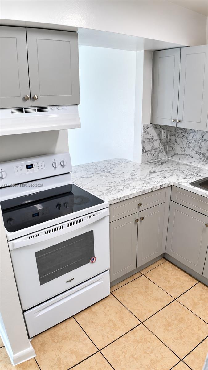 Kitchen featuring gray shaker-style cabinetry, patterned stone-finish countertops, tiled backsplash, and a white electric range