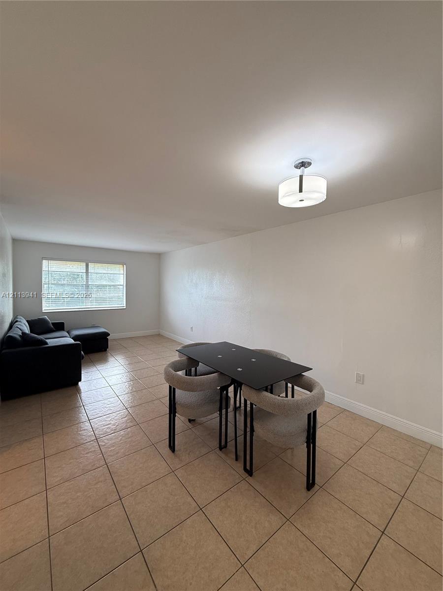 Open-concept room featuring neutral wall finishes, tile flooring, a large window, and a modern drum-style flush-mount ceiling light fixture Open-concept room featuring neutral wall finishes, tile flooring, a large window, and a modern drum-style flush-mount ceiling light fixture
