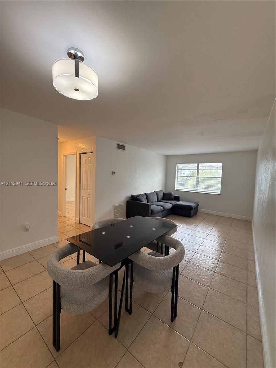 Open-concept room featuring light-toned tile flooring, a drum-style ceiling light fixture, and a large multi-pane window