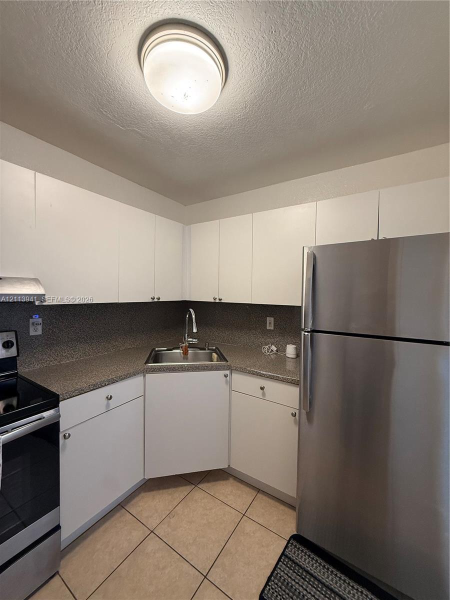 Kitchen featuring white cabinetry, speckled stone-finish countertops, stainless steel appliances, corner-mounted sink, and neutral tile flooring