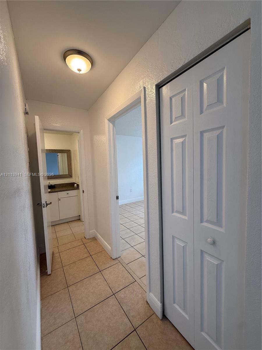 Hallway featuring neutral tile flooring, a six-panel bifold closet door, and a flush-mount dome light fixture
