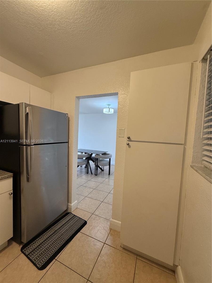 Kitchen featuring stainless steel refrigerator, tall pantry cabinetry, tile flooring, and window blinds