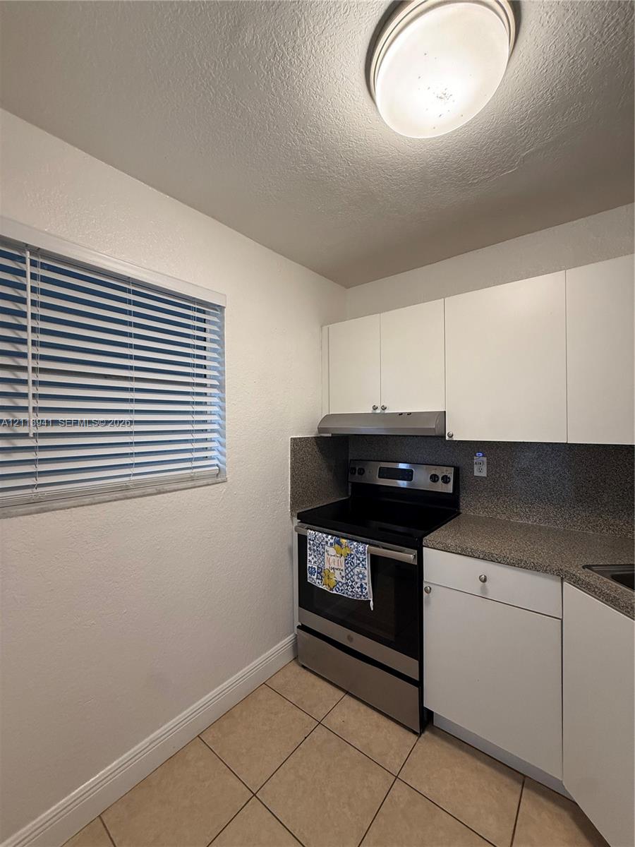 Kitchen featuring white flat-panel cabinetry, stone-finish countertops, stainless steel range, matching range hood, and tile flooring