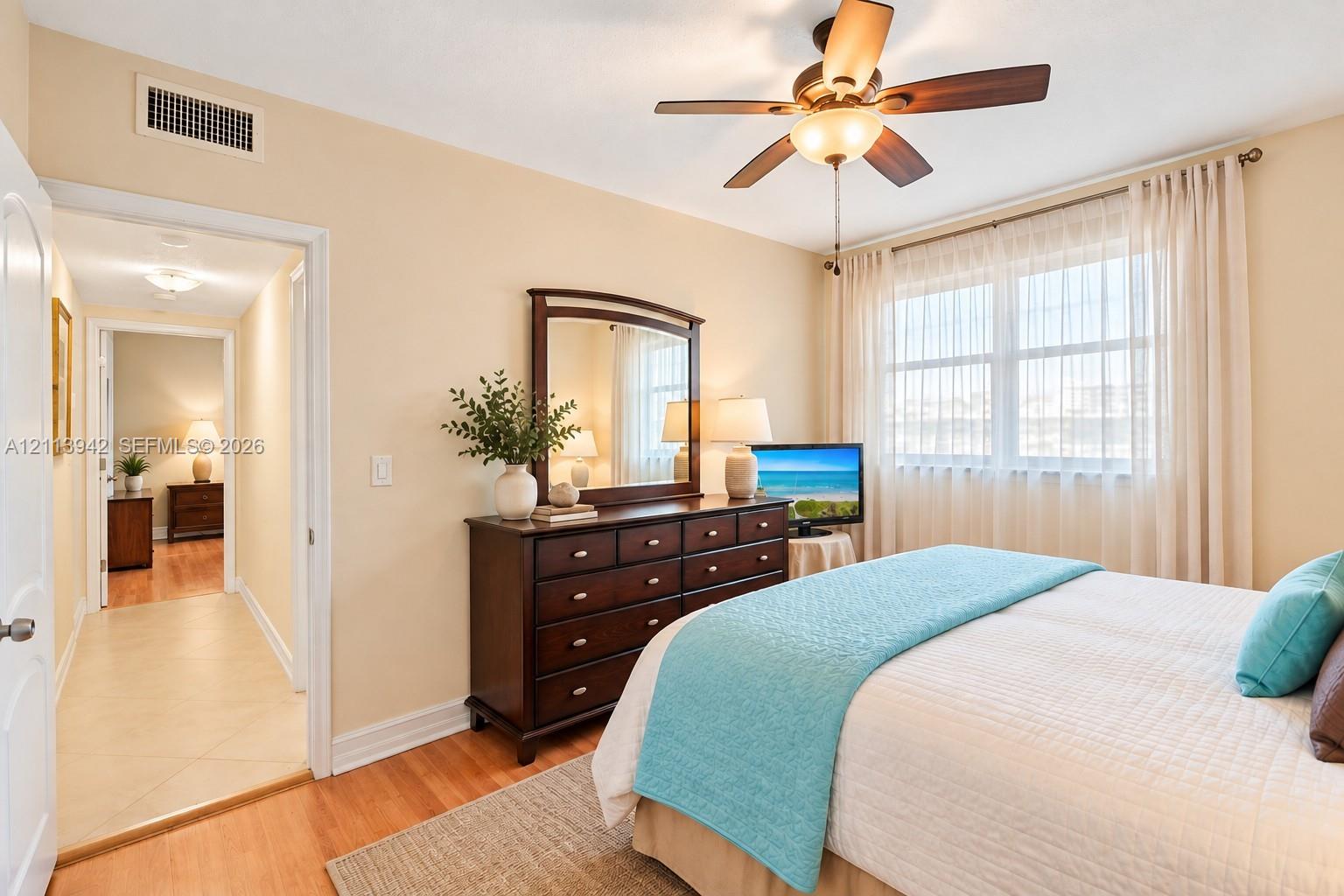 Room featuring wood-finish flooring, a multi-blade ceiling fan with integrated lighting, and a large window with horizontal blinds