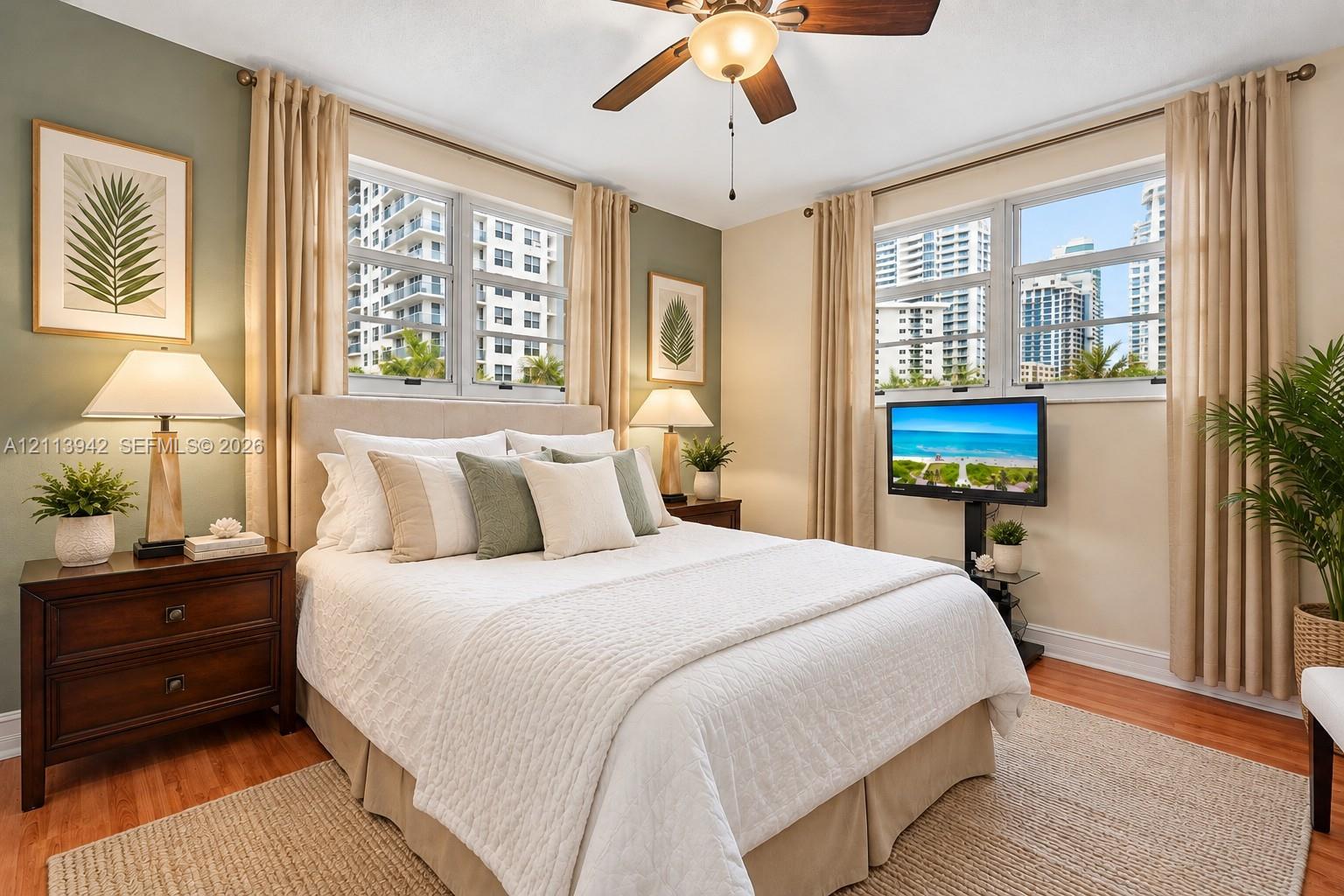 Bedroom featuring wood-finish flooring, dual-aspect windows, and a ceiling fan with integrated lighting