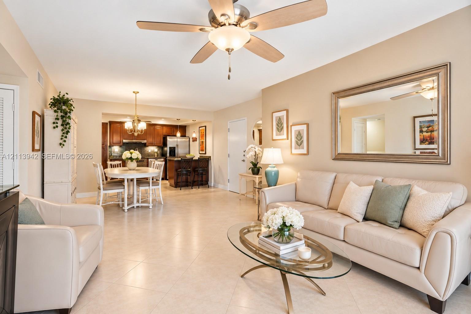 Open-concept interior featuring large-format tile flooring, a central ceiling fan with integrated lighting, recessed cabinetry, and a breakfast bar