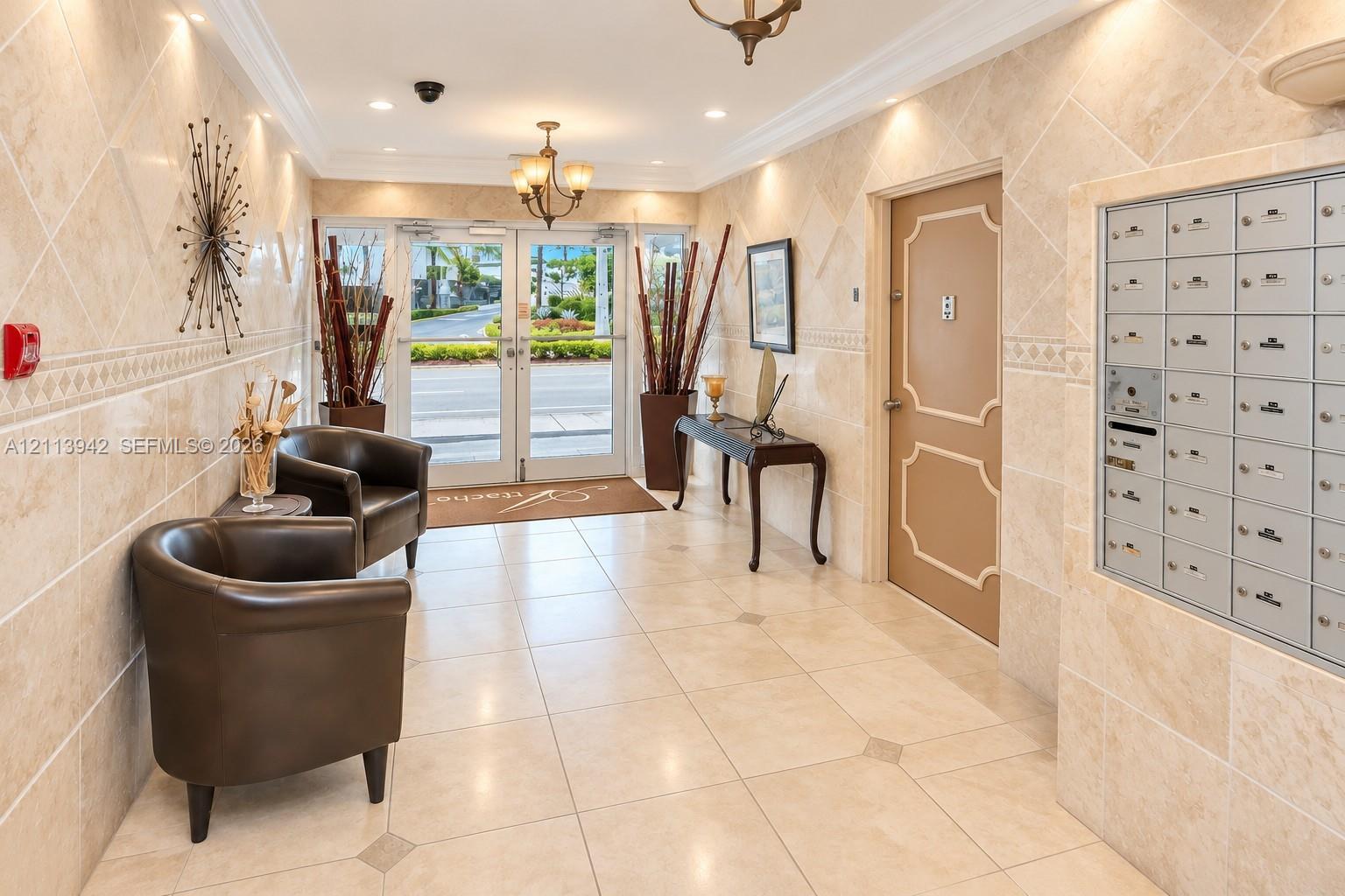 Lobby entrance featuring large-format tile flooring with decorative inserts, floor-to-ceiling stone wall cladding, built-in recessed parcel and mailboxes, and multi-light hanging chandeliers