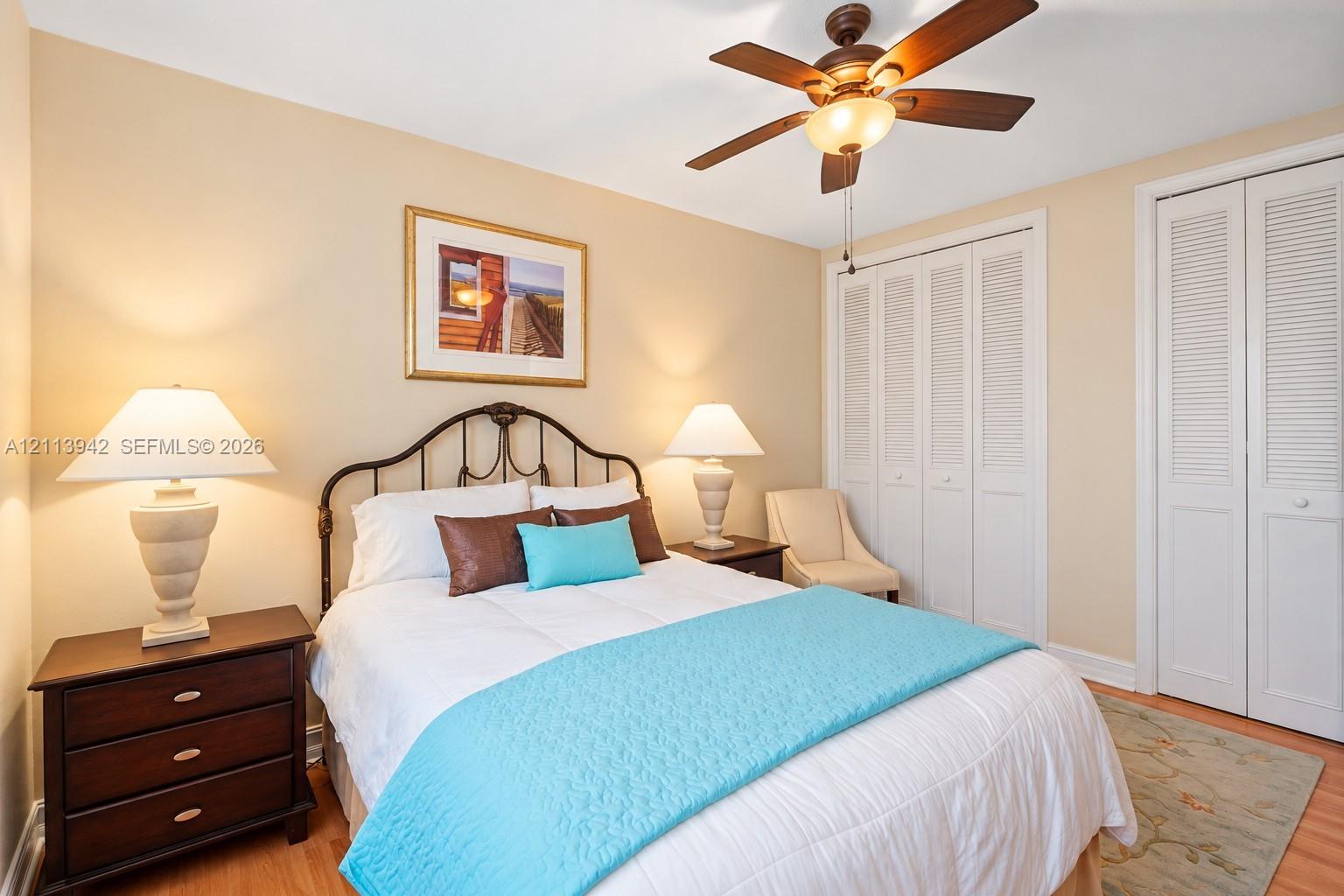 Neutral-toned interior featuring wood-finish flooring, a ceiling fan with integrated light fixture, and dual white louvered-panel closets