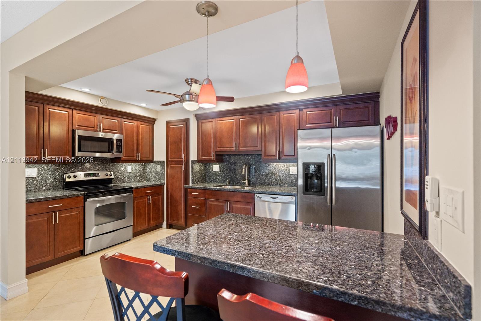 Kitchen featuring dark-toned cabinetry, stone countertops, stainless steel appliances, a center island with bar seating, and pendant lighting