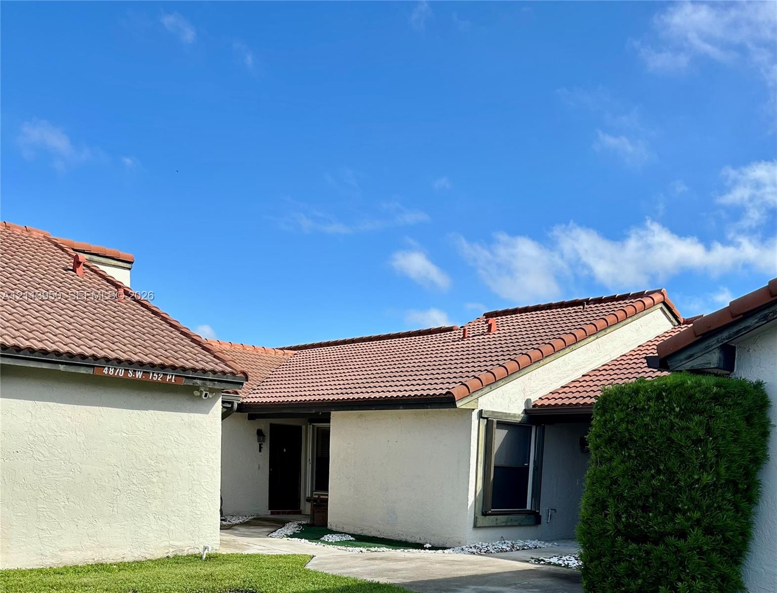 Stucco exterior featuring a multi-gabled clay tile roof, recessed entryway, and concrete walkway