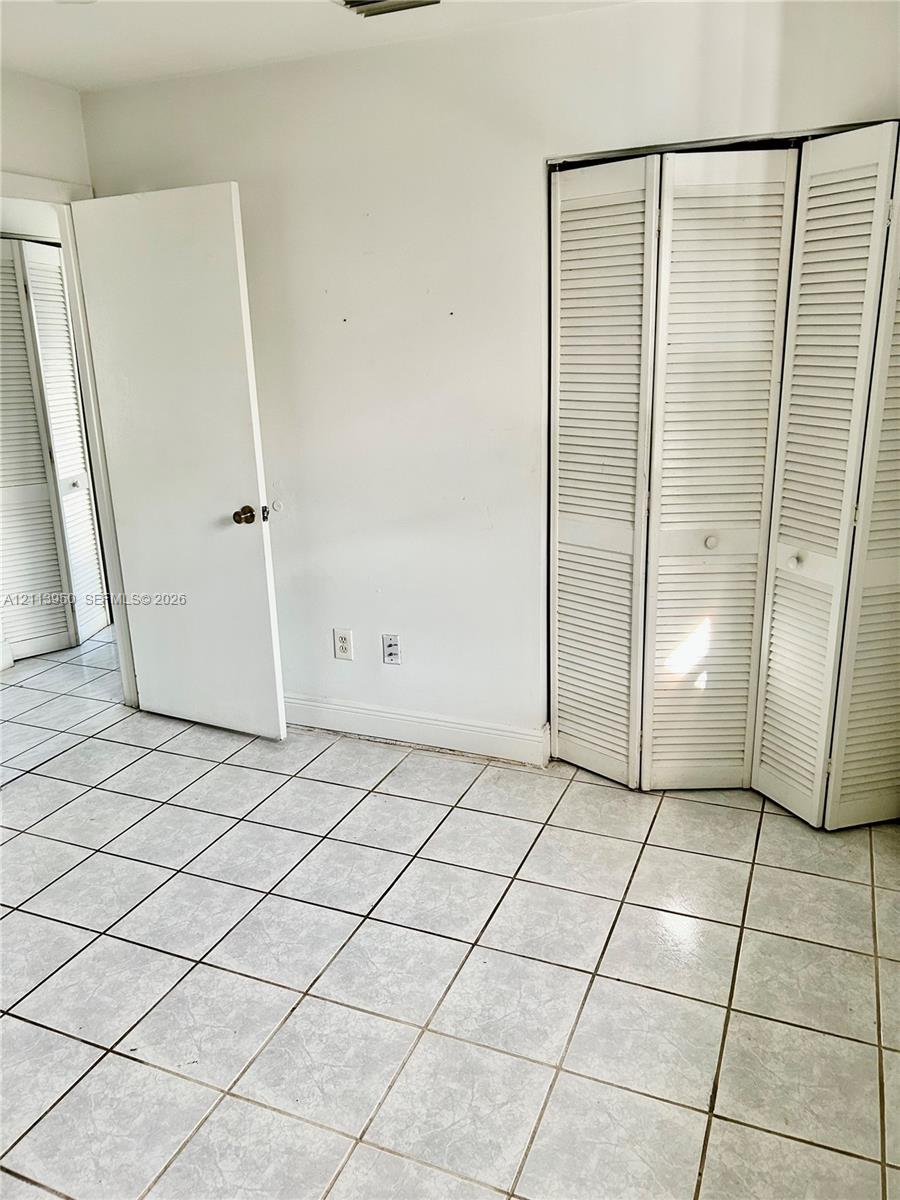 Neutral-toned tile flooring, white accordion-style louvered closet doors, and interior paneled doors Neutral-toned tile flooring, white accordion-style louvered closet doors, and interior paneled doors