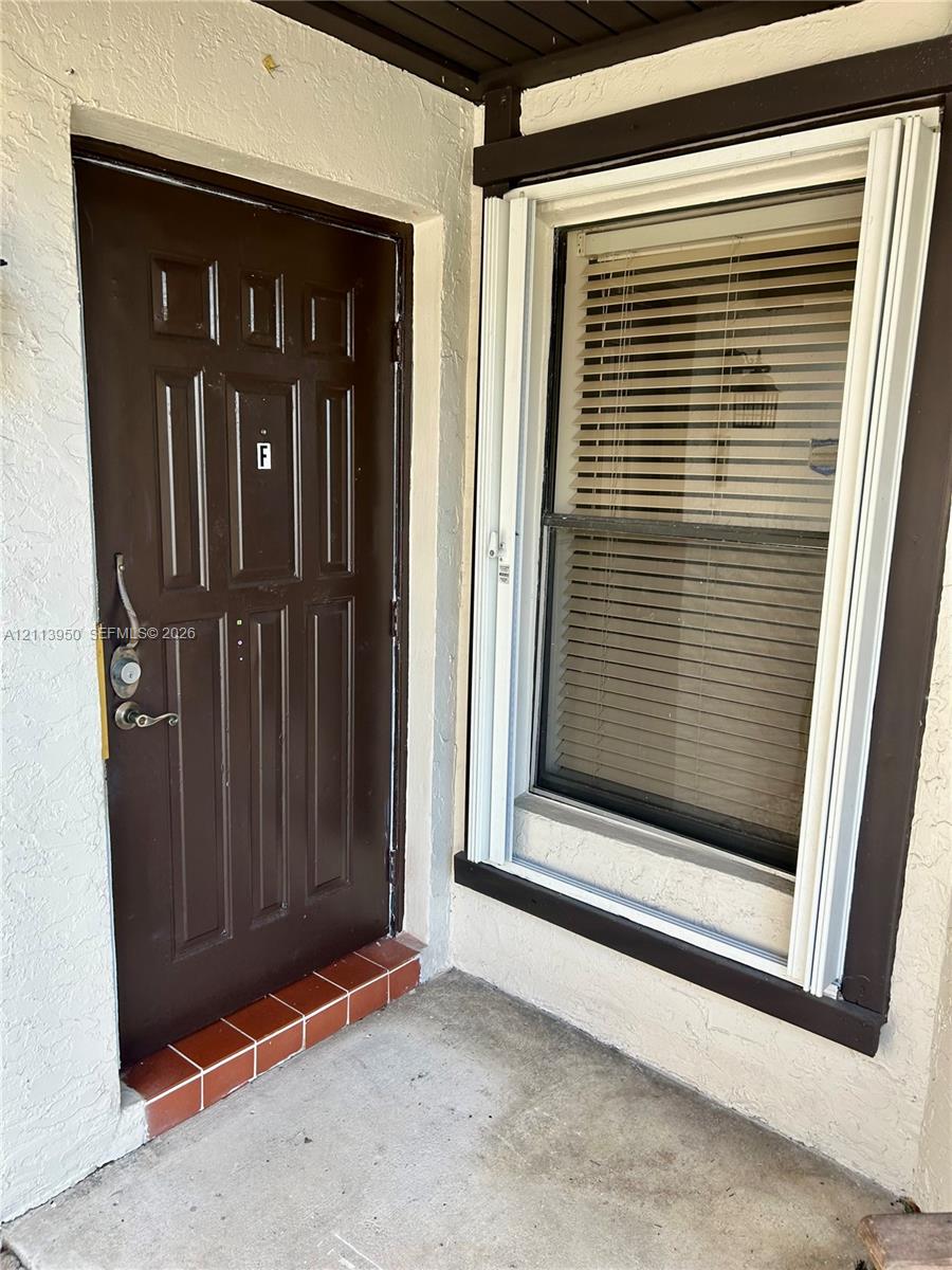 Exterior entry featuring a six-panel door, metal hardware, terracotta-tiled threshold, and window with white trim Exterior entry featuring a six-panel door, metal hardware, terracotta-tiled threshold, and window with white trim