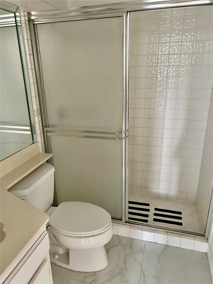 Bathroom featuring a shower stall with a sliding glass door and tiled surround, white vanity, and stone-finish flooring Bathroom featuring a shower stall with a sliding glass door and tiled surround, white vanity, and stone-finish flooring