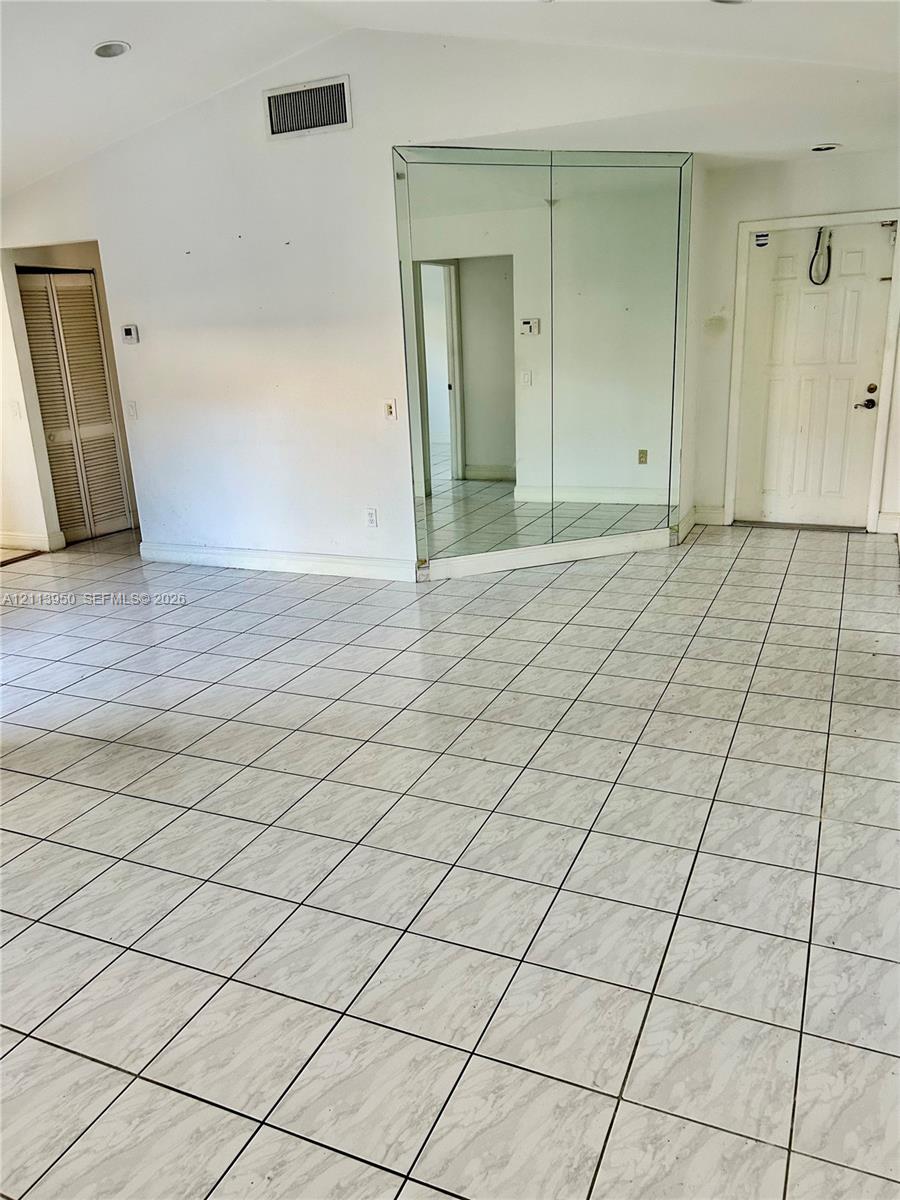 Vaulted ceilings with recessed lighting, large-format tiled flooring, floor-to-ceiling mirrored wall paneling, and bi-fold closet doors