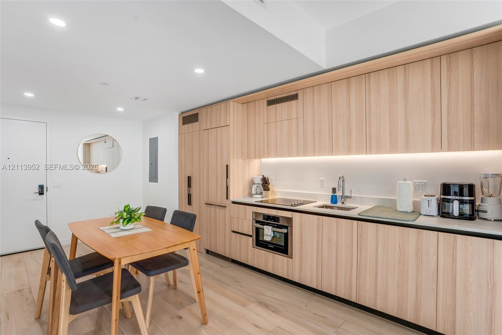 Modern kitchen featuring light wood-finish flat-panel cabinetry, integrated refrigerator, recessed lighting, and wood-finish flooring