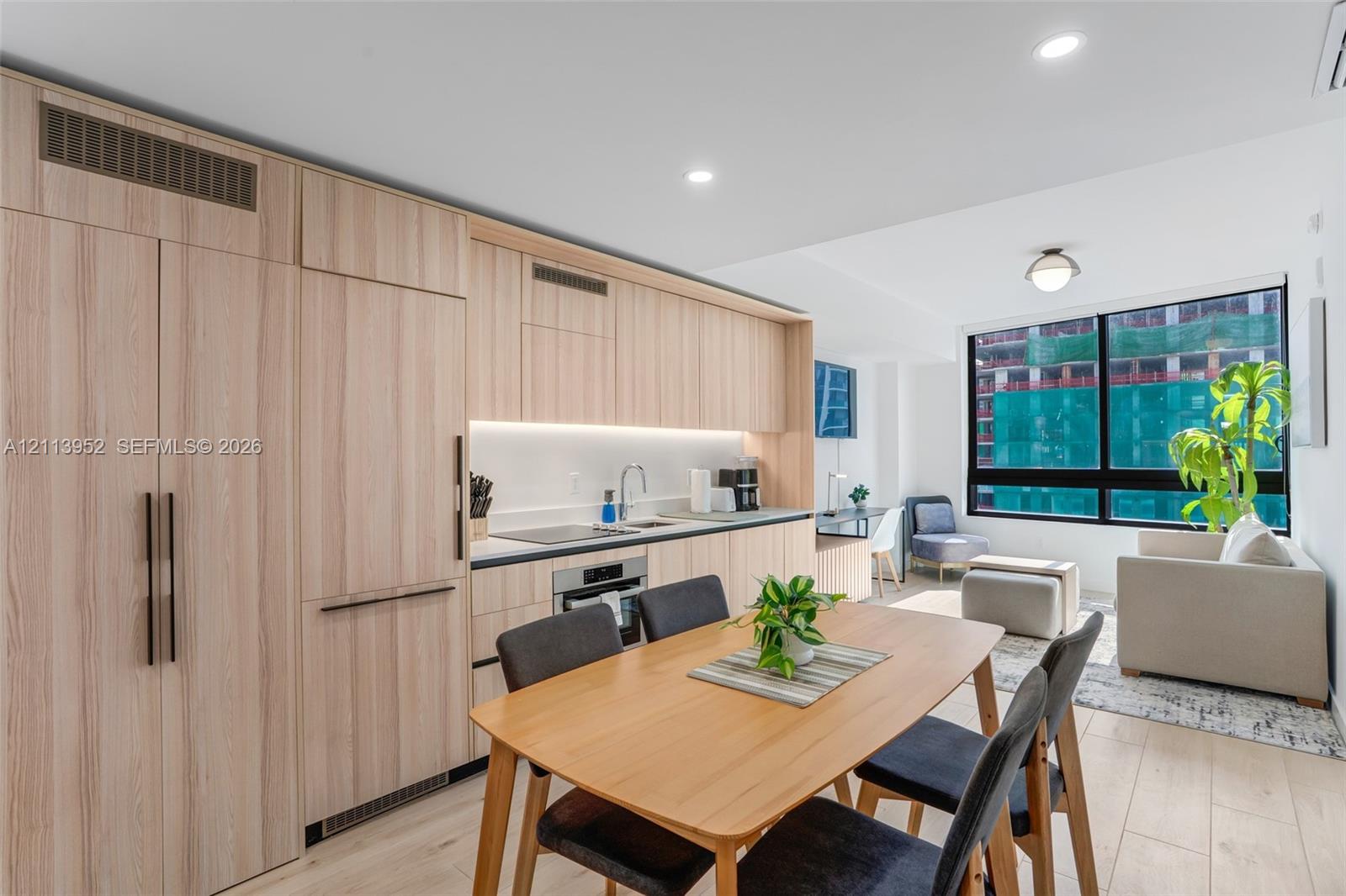 Kitchen featuring light wood-finish cabinetry with integrated appliances, solid surface countertops, recessed ceiling lighting, and expansive floor-to-ceiling windows