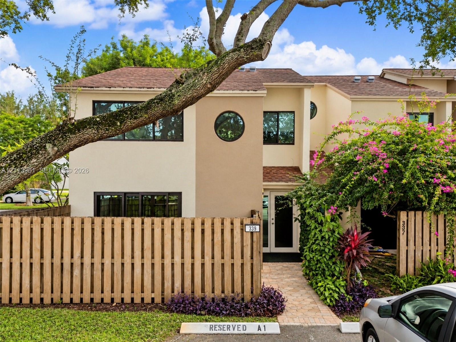 Exterior facade featuring a two-story stucco finish, prominent circular accent window, shingle roofing, and a private wooden privacy fence Exterior facade featuring a two-story stucco finish, prominent circular accent window, shingle roofing, and a private wooden privacy fence