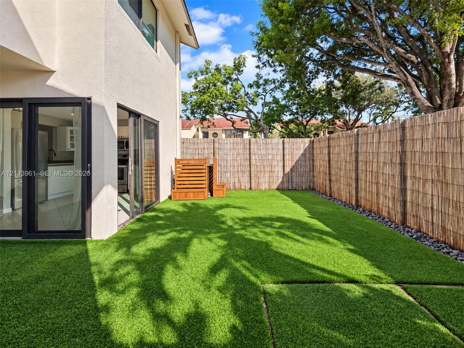 Private fenced backyard featuring artificial turf, river rock landscaping borders, and multi-panel sliding glass doors