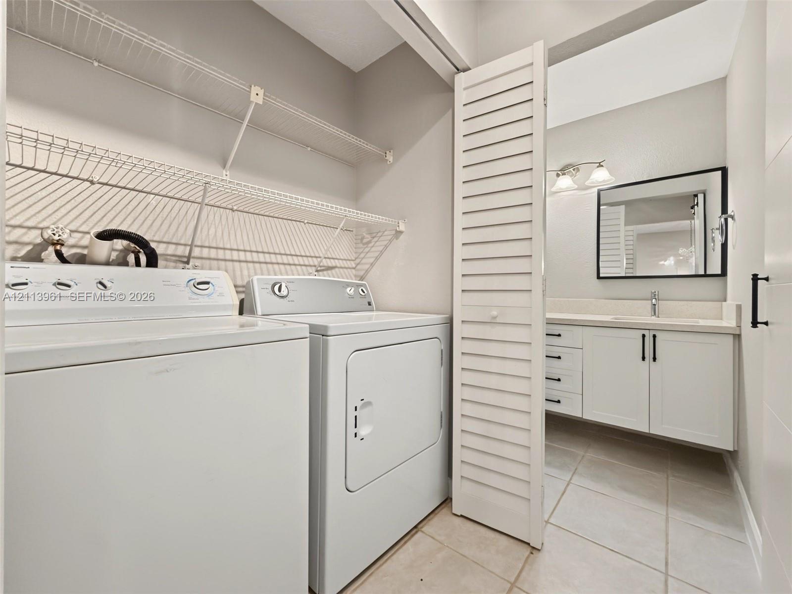 Laundry area featuring wire shelving and white cabinetry with a vanity including a rectangular sink, stone-finish countertop, black hardware, and a framed mirror