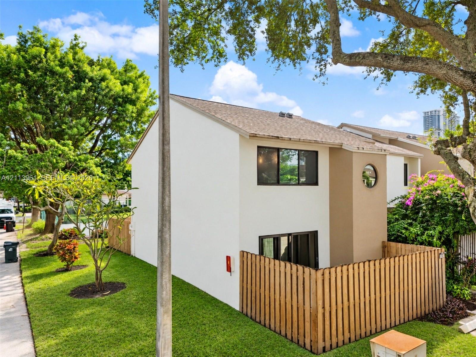 Two-story exterior featuring a neutral-toned stucco finish, wood-plank privacy fencing, an accent circular window, and mature landscaping Two-story exterior featuring a neutral-toned stucco finish, wood-plank privacy fencing, an accent circular window, and mature landscaping