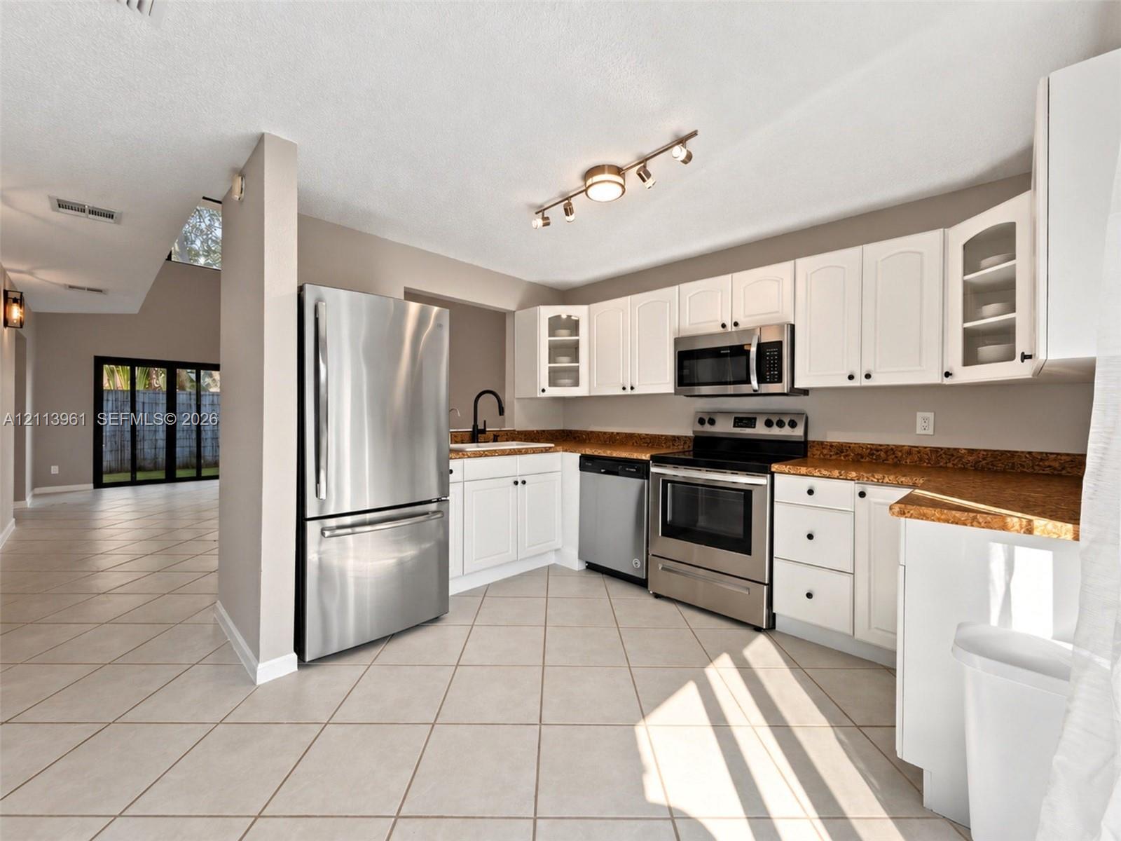 Kitchen featuring white cabinetry with glass-panel display doors, stainless steel appliances, stone-finish countertops, ceramic tile flooring, and multi-directional track lighting