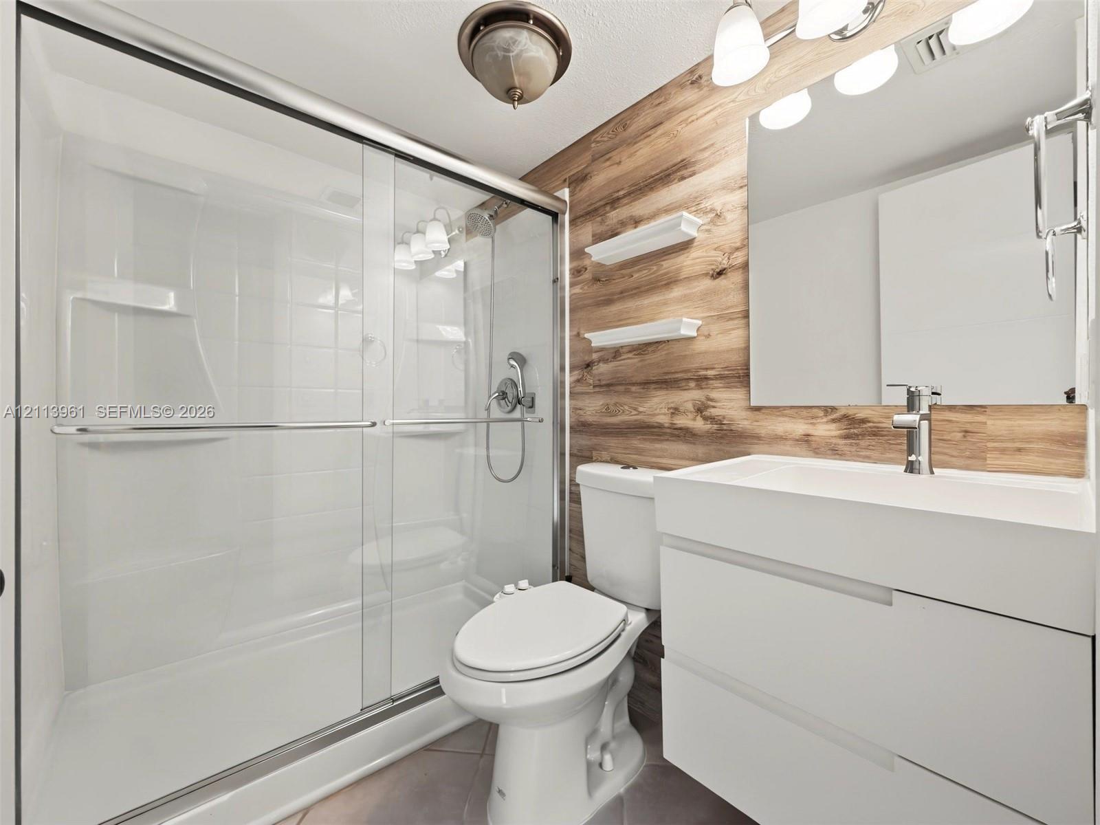 Bathroom featuring a floating vanity with a rectangular sink, wood-finish wall paneling, a glass-enclosed shower with chrome fixtures, and built-in wall shelving Bathroom featuring a floating vanity with a rectangular sink, wood-finish wall paneling, a glass-enclosed shower with chrome fixtures, and built-in wall shelving