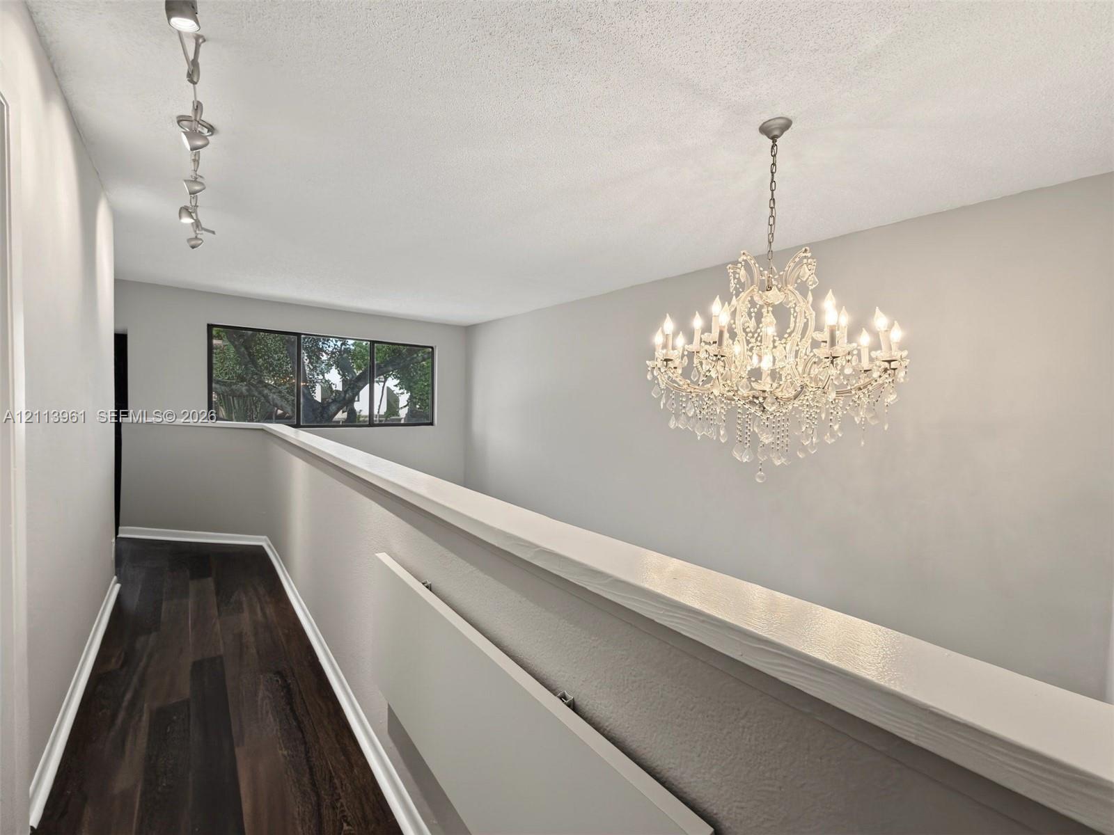 Wood-finish flooring, ornate crystal chandelier, track lighting, and window with natural greenery exposure