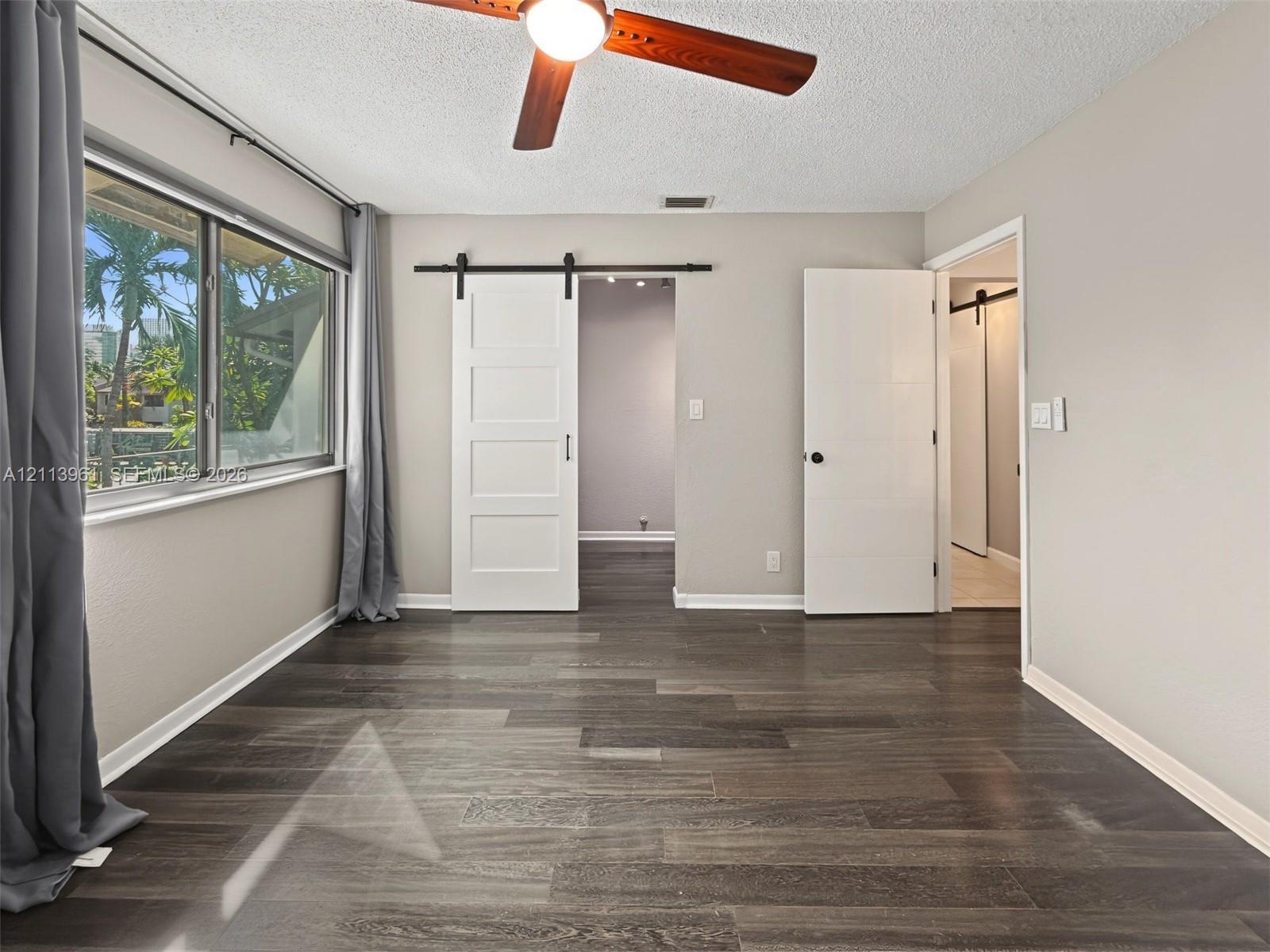 Wood-finish flooring, white four-panel sliding barn door, ceiling fan, and multi-pane horizontal window