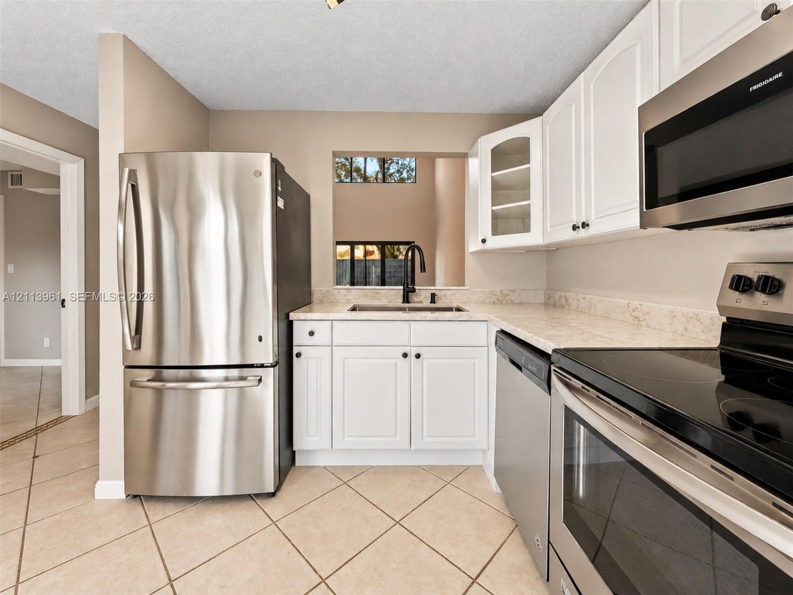 Kitchen featuring stainless steel appliances, white cabinetry with glass-panel accents, stone-composite countertops, and neutral tile flooring