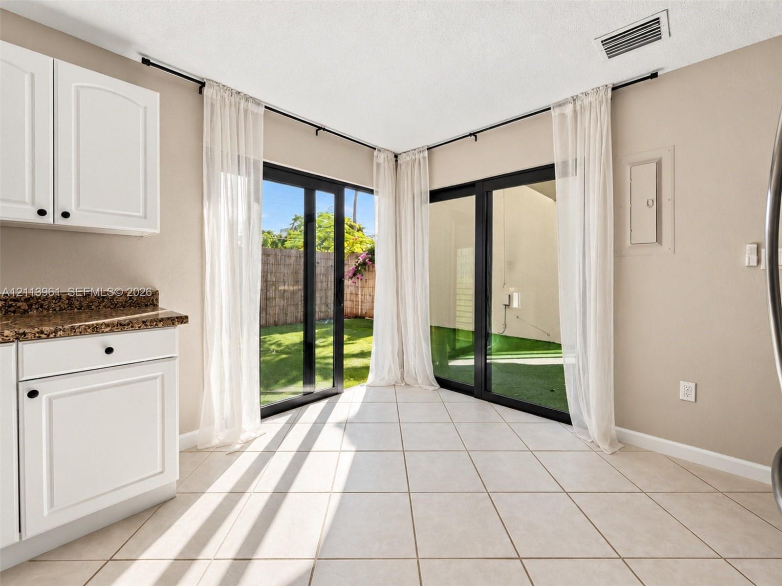 Dual sliding glass doors, white cabinetry, stone-finish countertops, and light-toned tile flooring