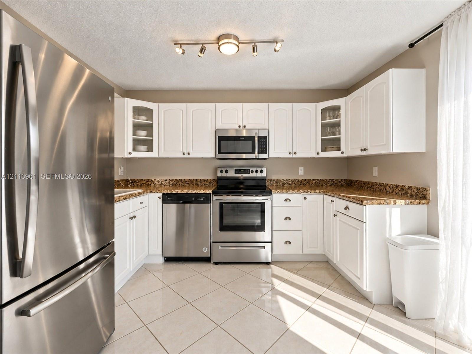Kitchen featuring white cabinetry, stone-finish countertops, stainless steel appliances, ceramic tile flooring, and multi-directional track lighting