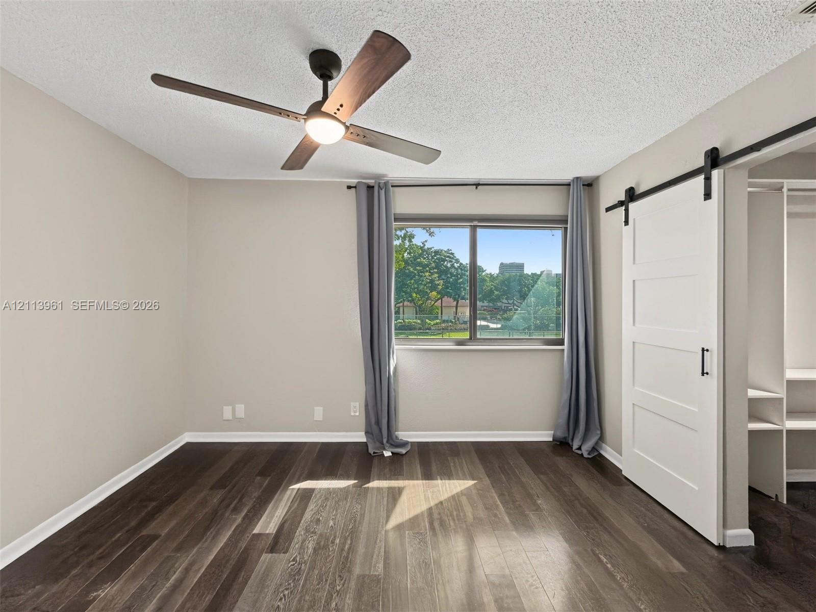Wood-finish flooring, white sliding barn door, integrated shelving, modern ceiling fan with light fixture, and single-pane window