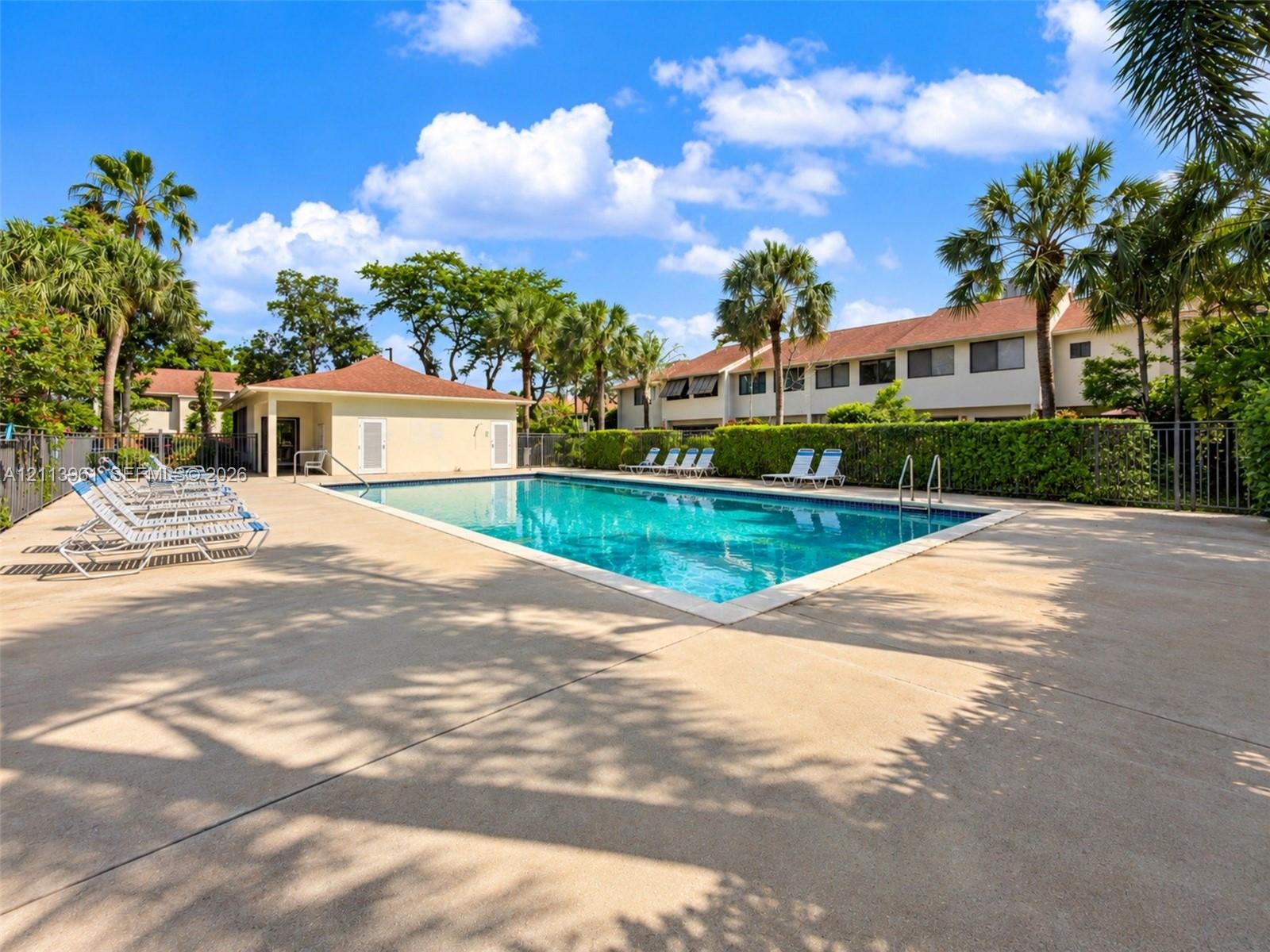 Swimming pool with a concrete deck, pool house, and surrounding mature landscaping